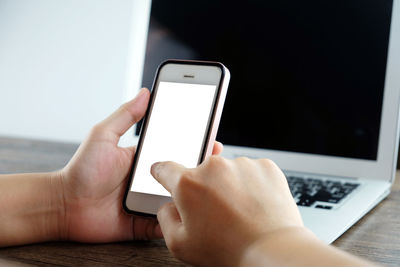 Cropped hands of woman using mobile phone at table