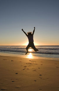 Silhouette people jumping at beach against sky during sunset