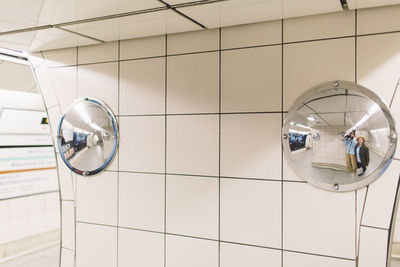 Reflection of man and woman on road mirror mounted to tiled wall at underground walkway