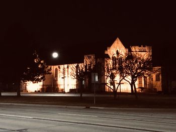 Illuminated street by buildings against clear sky at night