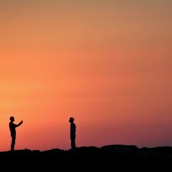 Silhouette of people standing on landscape at sunset