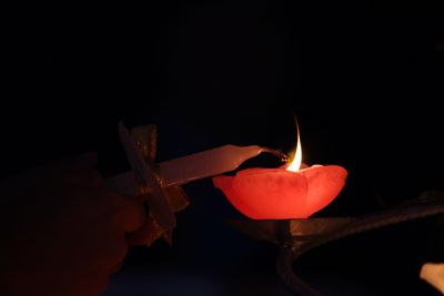 Close-up of hand holding burning candle against black background