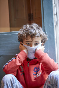 Close-up portrait of boy wearing mask sitting against door