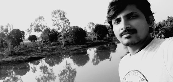 Portrait of young man by lake against sky