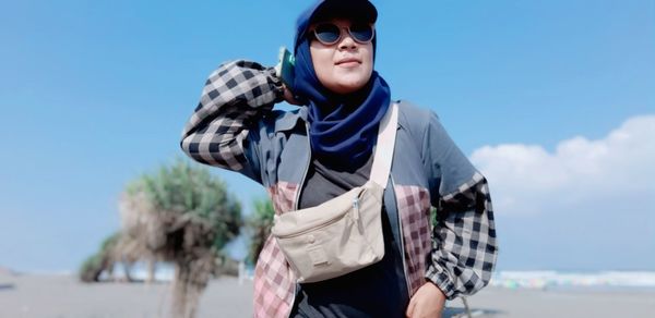 Young woman wearing sunglasses standing against blue sky