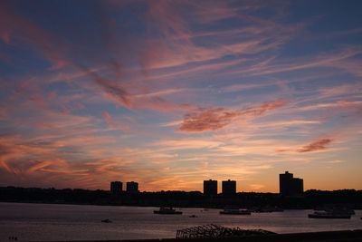 Silhouette buildings by sea against sky during sunset