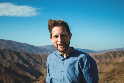 Portrait of young man standing on mountain against blue sky