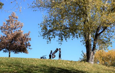 People on field by trees against sky