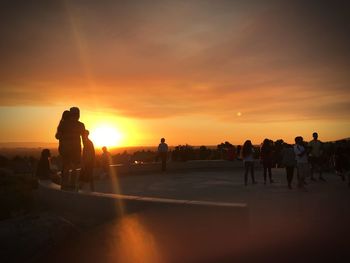 People standing at observation point against orange sky during sunset