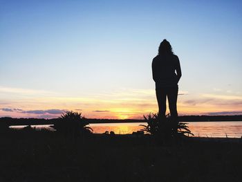 Silhouette woman standing on beach against sky during sunset