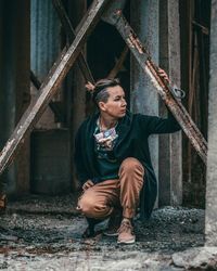 Man looking away while crouching by rusty metallic structure