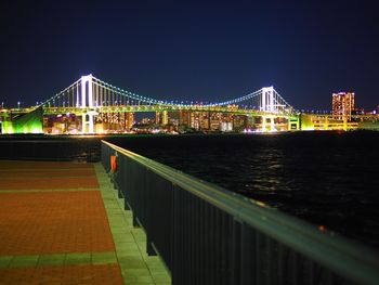 Illuminated bridge over river with buildings in background