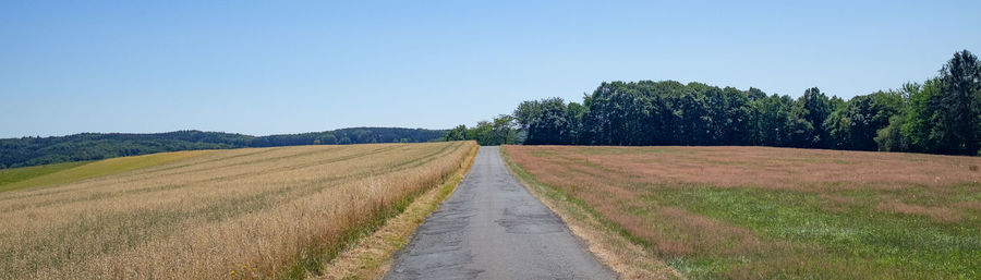 Dirt road amidst field against clear sky