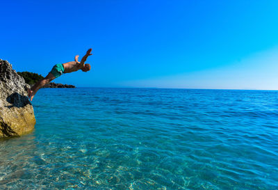 Man diving in sea against clear blue sky