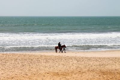 Men standing on beach against clear sky