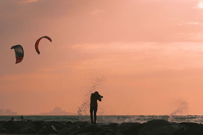 Silhouette man photographing at beach against sky during sunset