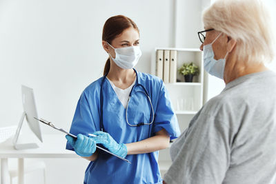 Side view of female doctor holding dentures while standing against white background