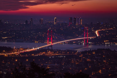 Illuminated city by river against sky at night