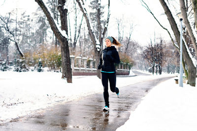 Woman running on snowy field against bare trees