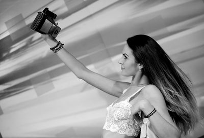 Young woman taking selfie from camera while leaning on retaining wall