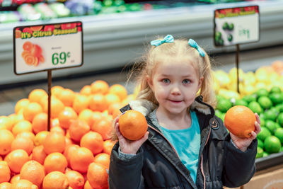 Cute girl holding orange standing in supermarket