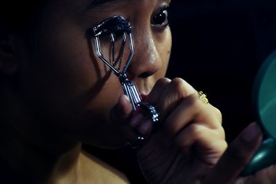 Close-up of woman using eyelash curler while looking at mirror