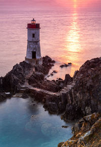 High angle view of lighthouse on rock formation by sea during sunset