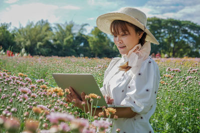 Smiling woman using laptop while standing on field against sky