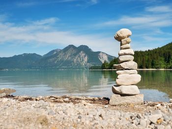 Pyramid of flat stones on a pebbly lake beach, the mountains mirroring in smooth water level.