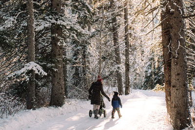 Rear view of mother and son walking in forest during winter