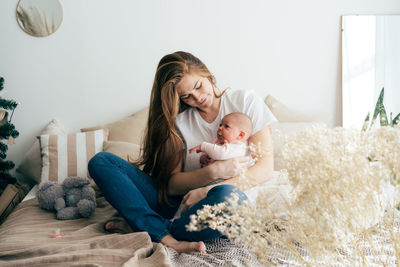 A tender caring mother nurses a newborn baby in her arms while sitting on the bed.