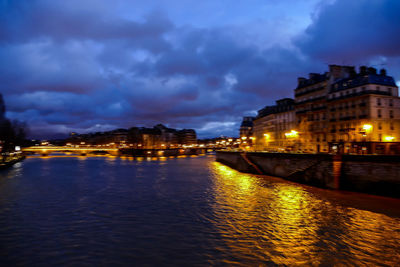 Illuminated buildings by river against sky