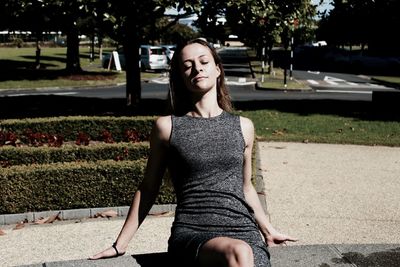 Woman with closed eyes sitting on retaining wall at park