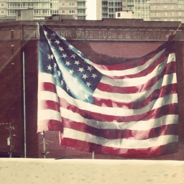 patriotism, flag, identity, building exterior, american flag, national flag, architecture, built structure, red, striped, culture, city, white color, day, road, street, outdoors, wind, pride, no people