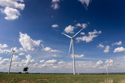 Low angle view of windmills on field against cloudy sky