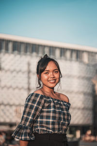 Portrait of smiling young woman standing against building and sky