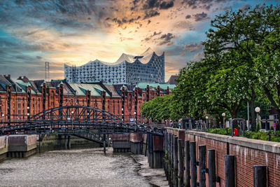 Bridge by buildings against sky during sunset