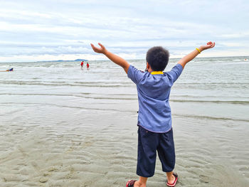 Rear view of boy standing at beach against sky