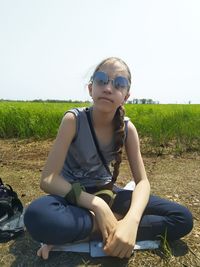 Young woman wearing sunglasses sitting on field