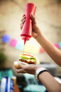 Cropped image of woman pouring ketchup on hamburger at garden party