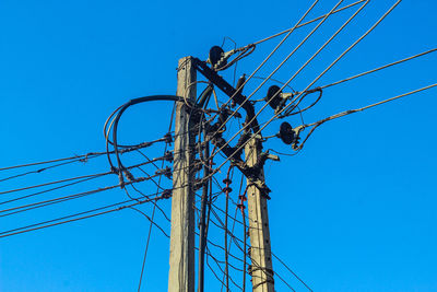 Low angle view of electricity pylon against clear blue sky