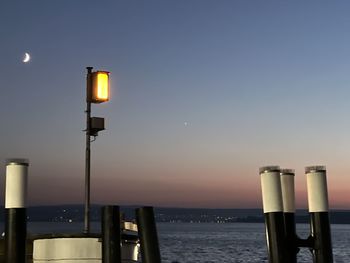 Illuminated street light by sea against clear sky