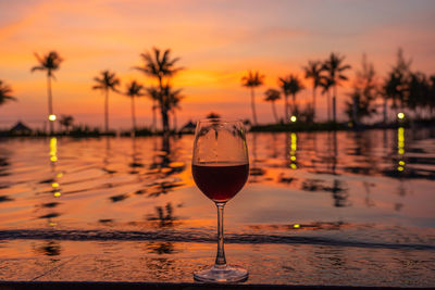 Glass of red wine with reflection of palm trees against sky during sunset