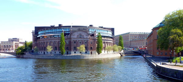 View of buildings by river against sky in city