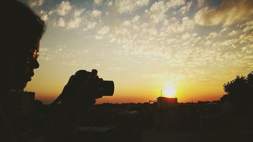 Silhouette man photographing cityscape against sky during sunset