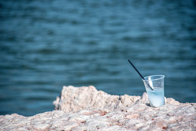 Plastic cup cocktail with a straw abandoned on the rocks by the seaside.