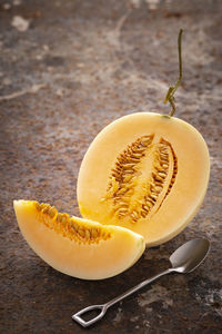 Sliced yellow cantaloupe melon with dessert spoon on rusty texture background