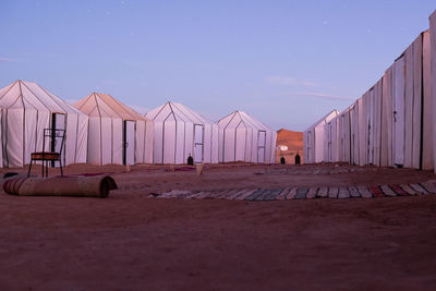 Lots of white tents chair and carpets on sand with clear blue evening sky on background in morocco
