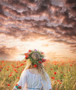 Rear view of woman standing on field against cloudy sky