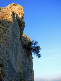 Low angle view of rocky mountain against clear blue sky